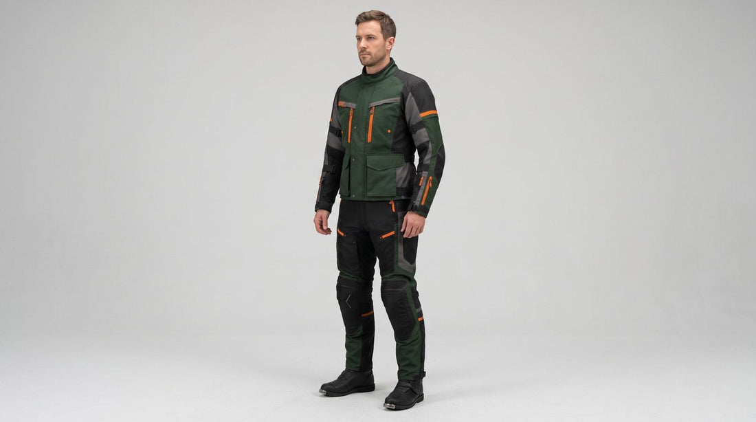 Rider wearing a forest green, grey and black adventure textile motorcycle suit with orange zips on a light grey studio background
