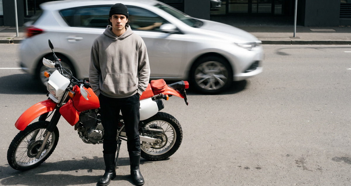 Rider standing beside an enduro motorcycle as traffic blurs past, in black leather boots