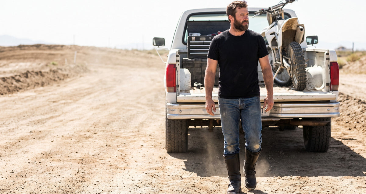Rider walking past a pickup tailgate at a dirt track in tall black racing boots