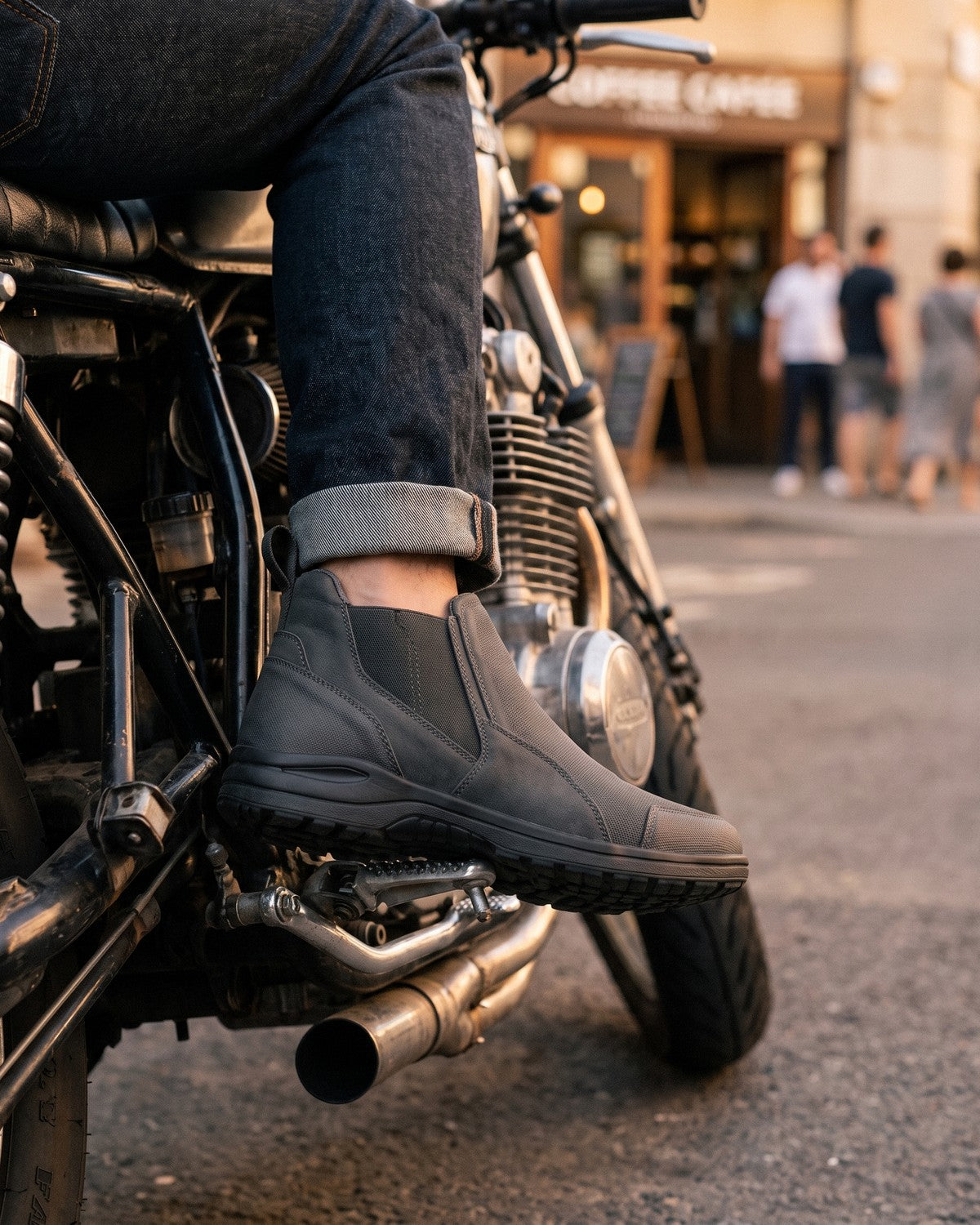 Grey slip-on riding shoes on the pegs of a parked cafe racer