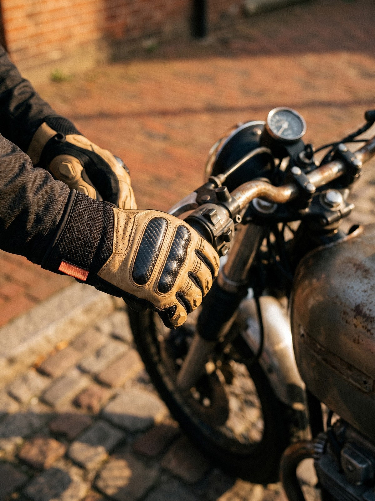 Gloved hands on the bars of a cafe racer in warm street light