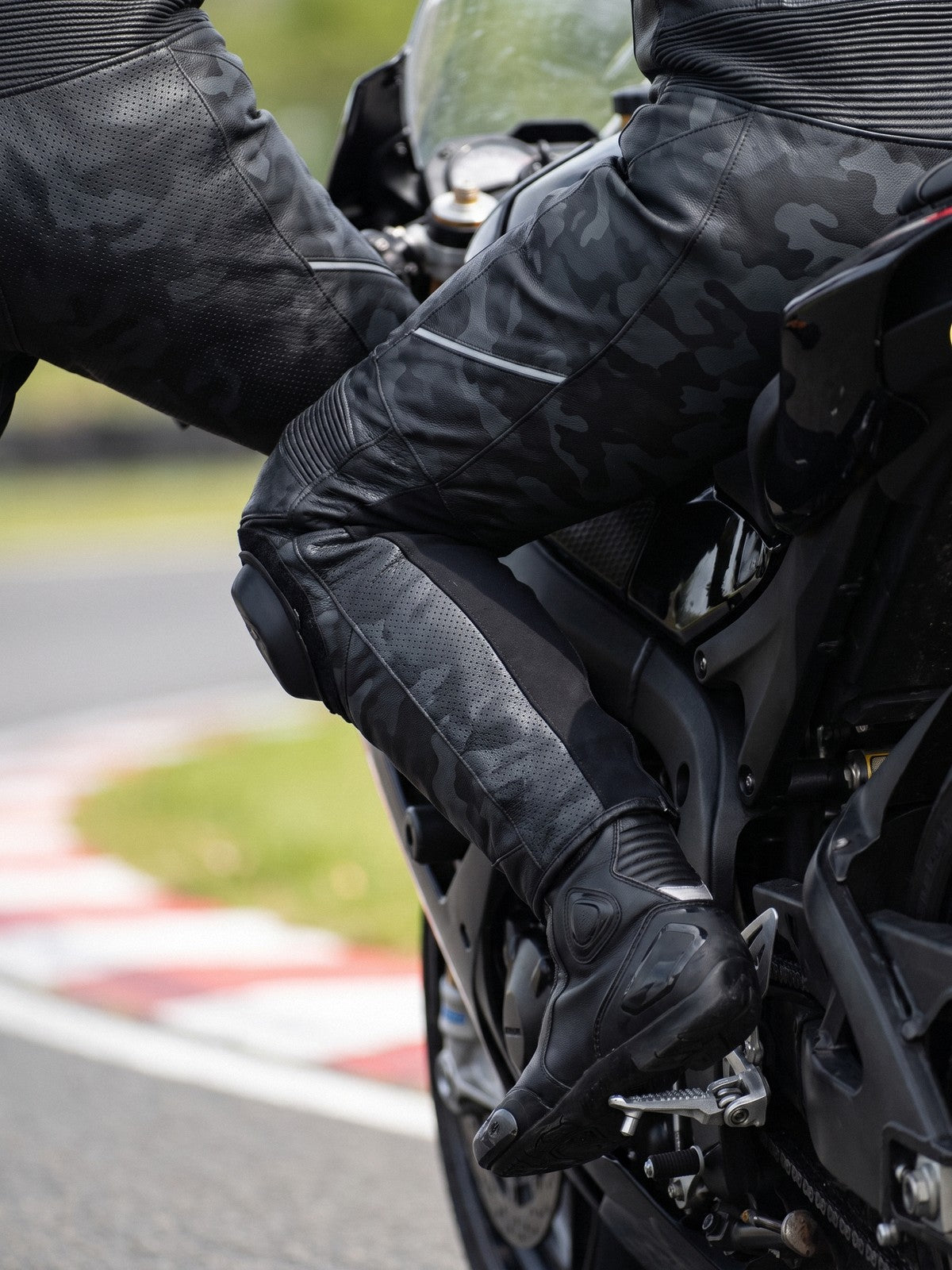 Racer's legs in black leather racing trousers astride a sportbike at trackside
