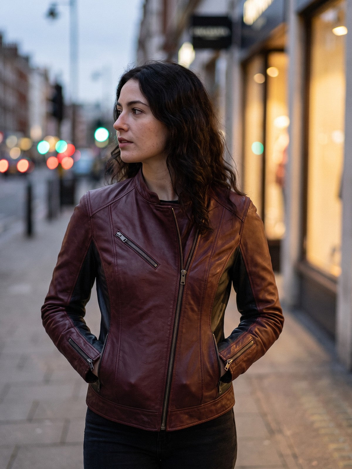 Woman in a burgundy leather street jacket on a city pavement at dusk