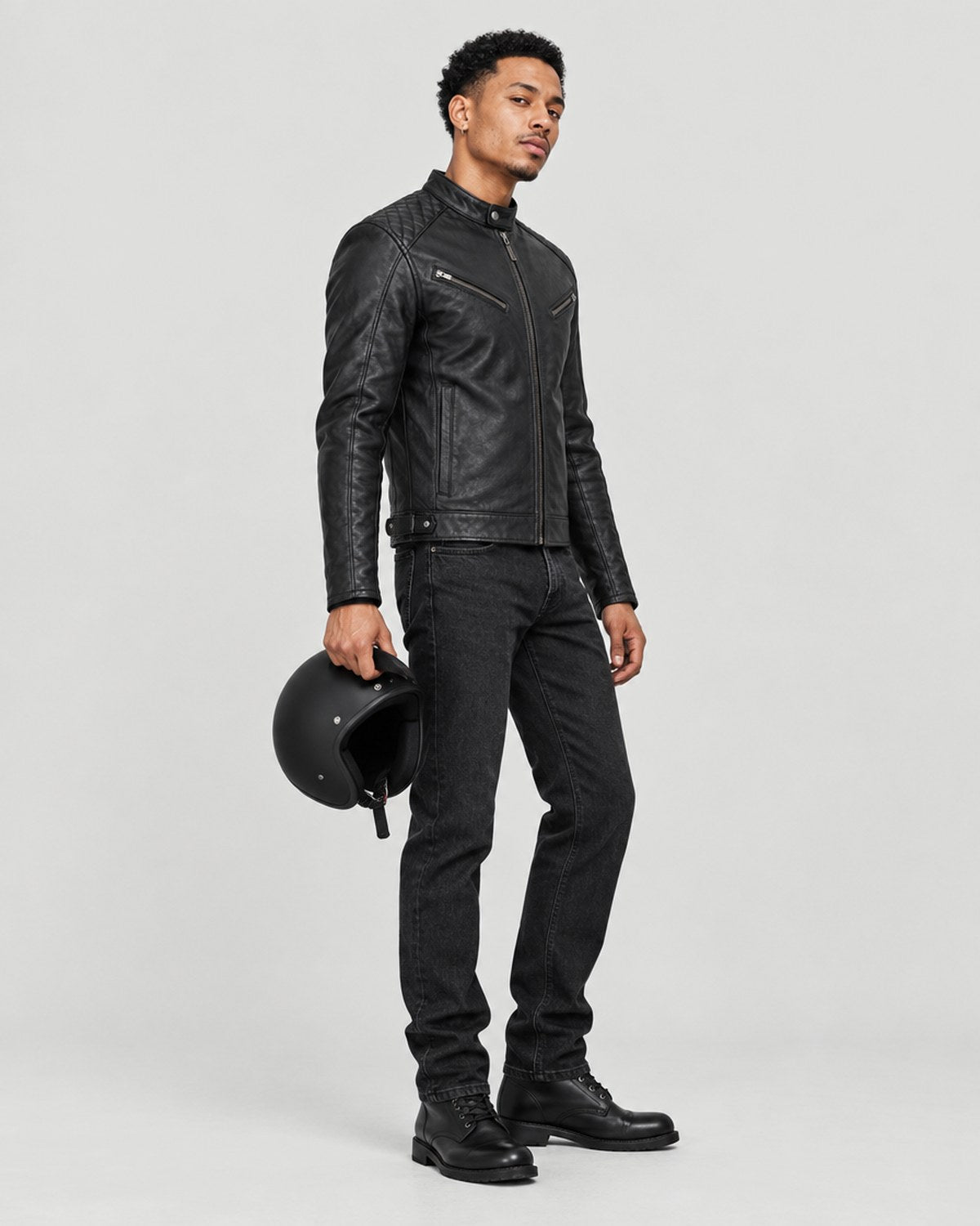 Model in the Asphalt Nomad leather jacket holding a helmet in a grey studio