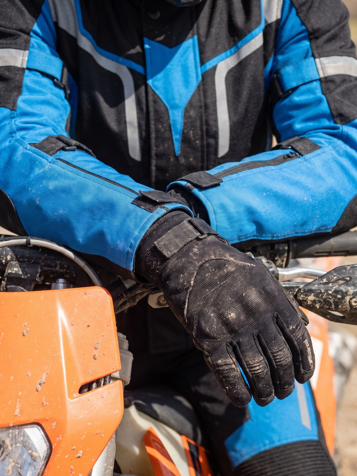 Gloved forearms crossed on a handlebar in a black and blue women's textile jacket